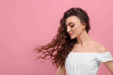 Beautiful young woman with long curly brown hair on pink background, space for textの写真素材