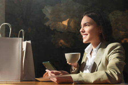 Special Promotion. Happy young woman with cup of drink using smartphone at table in cafeの写真素材