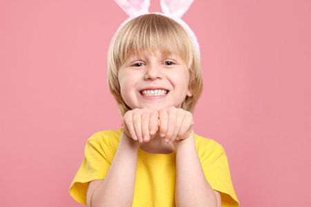Happy boy wearing bunny ears headband on pink background. Easter celebration