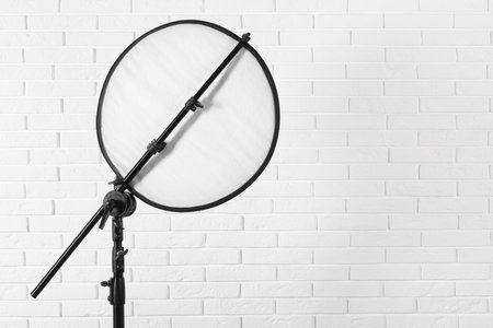Professional light reflector on tripod against white brick wall, space for text. Photography equipmentの写真素材
