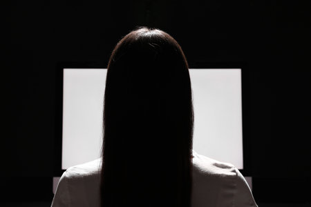 Woman using computer in dark room, back view. Internet addictionの写真素材