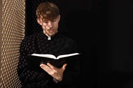 Catholic priest with Bible near wooden window in confessional. Space for textの写真素材