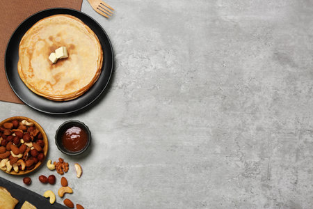 Delicious crepes with butter, chocolate and different nuts on light gray table, flat lay. Space for...