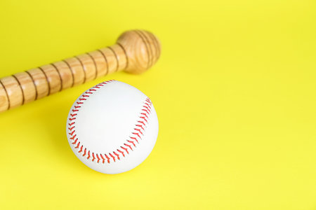 Wooden baseball bat and ball on yellow background, space for text. Sports equipmentの写真素材