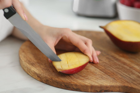 Woman preparing mango for tasty smoothie at white marble table, closeup