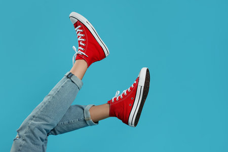 Woman in stylish gumshoes on light blue background, closeup. Space for textの写真素材