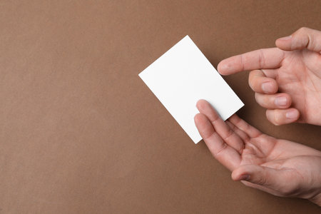 Man holding paper card on brown background, top view. Mockup for designの写真素材
