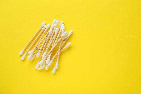 Heap of wooden cotton buds on yellow background, flat lay. Space for textの写真素材