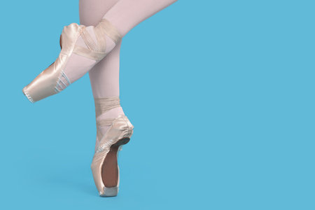 Young ballerina in pointe shoes practicing dance moves on light blue background, closeup. Space for textの写真素材