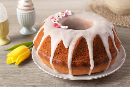 Delicious Easter cake decorated with sprinkles near beautiful tulip and painted eggs on wooden...