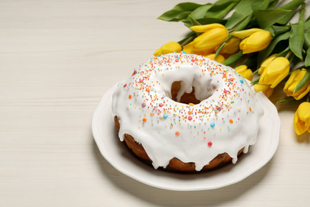 Easter cake with sprinkles and tulips on white wooden table, space for text
