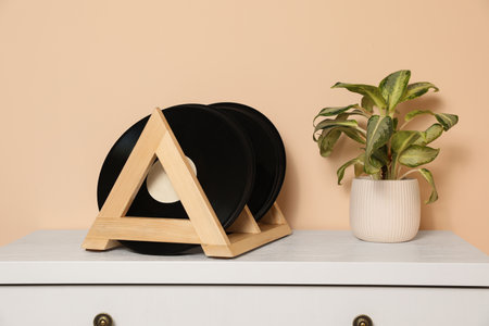 Vinyl records and potted plant on white wooden drawer dresser near beige wall