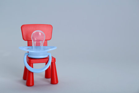 Maternity leave concept. Toy chair with baby pacifier on light gray background, space for textの写真素材