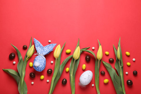 Flat lay composition with Easter bunny made of wrapping paper and egg on red background. Space for textの写真素材