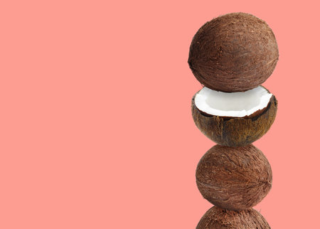Stack of fresh coconuts on coral color background. Space for textの写真素材