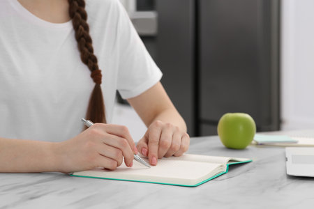 Woman writing in notebook at white marble table indoors, closeupの写真素材