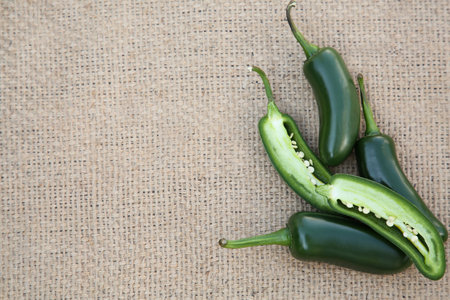 Whole and cut fresh green jalapeno peppers on sacking, flat lay. Space for text