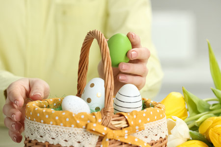 Closeup of woman putting painted egg into Easter basket