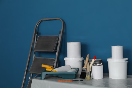 Metallic folding ladder and painting tools on table near blue wallの写真素材
