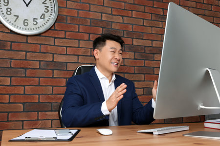 Happy boss having online meeting via computer at wooden table in modern officeの写真素材