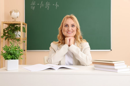Happy professor with books sitting at desk in classroomの写真素材