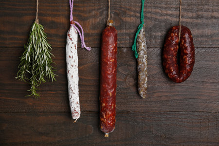 Different delicious sausages and bunch on rosemary hanging near wooden wallの写真素材