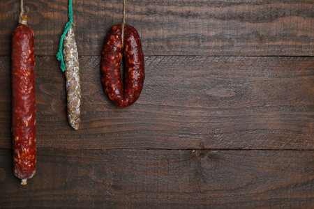 Different delicious sausages hanging near wooden wall. Space for textの写真素材