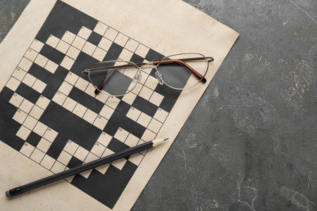 Blank crossword, glasses and pencil on gray table, top view. Space for textの写真素材