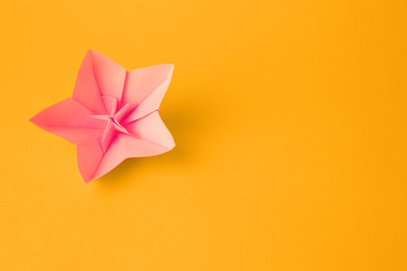 Origami art. Handmade pink paper flower on yellow background, top view with space for textの写真素材