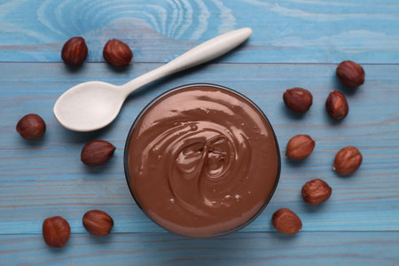 Bowl with tasty chocolate paste and nuts on light blue wooden table, flat layの写真素材