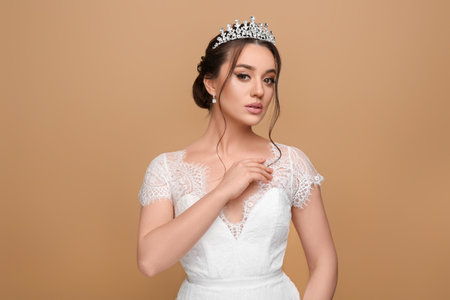 Beautiful young woman wearing luxurious tiara on beige backgroundの写真素材