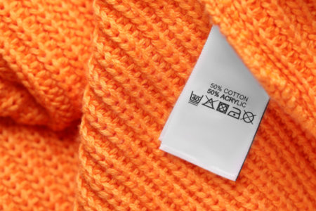 Clothing label with care recommendations on orange garment, top view. Space for textの写真素材