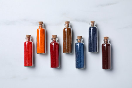 Glass bottles with different food coloring on white marble table, flat lay