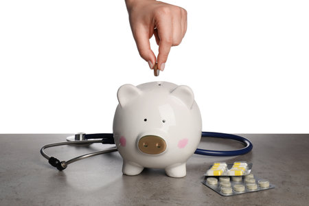 Woman putting coins into piggy bank on gray table against white background, closeup. medical insuranceの写真素材