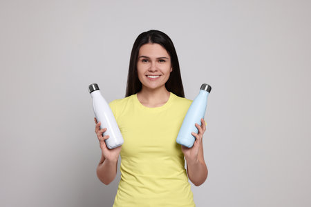 Young woman with thermo bottles on light gray backgroundの写真素材