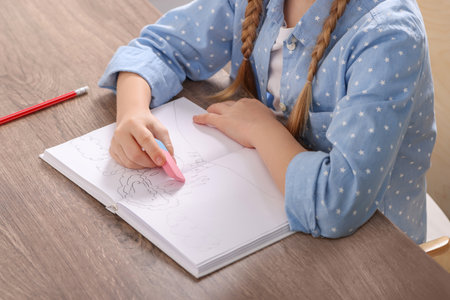 Girl erasing drawing in her book at wooden table, closeupの写真素材