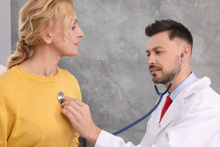 Doctor listening to patient's lungs with stethoscope in clinicの写真素材