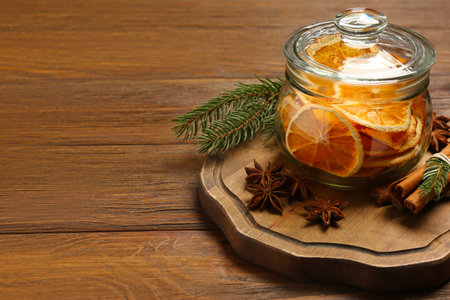 Glass jar of dry orange slices, anise stars, cinnamon sticks and fir branches on wooden table. Space for textの写真素材
