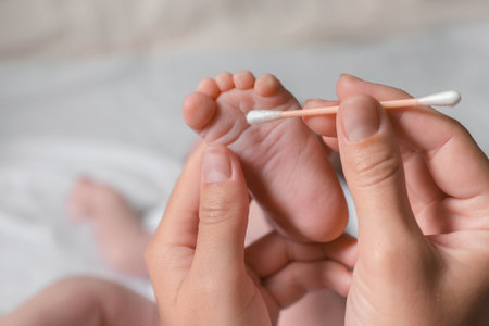 Mother cleaning baby`s foot with cotton bud on blurred background, closeupの写真素材