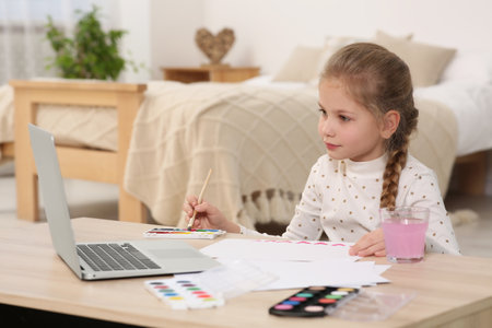 Little girl learning to paint with online course at home. Space for text