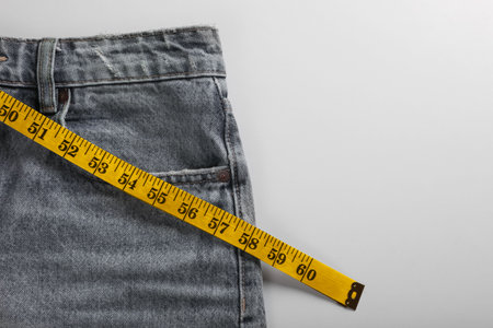 Jeans with measuring tape on light gray background, top view and space for text. weight loss conceptの写真素材