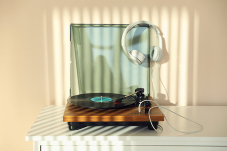 Stylish turntable with vinyl disc and headphones on white chest of drawers at homeの写真素材