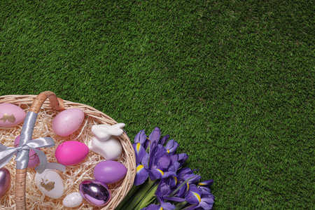 Easter basket with painted eggs, figure of rabbit and iris flowers on green grass, flat lay. Space for textの写真素材