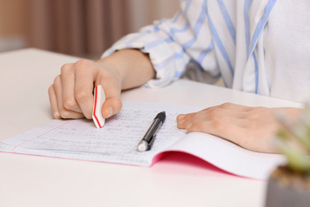 Girl erasing mistake in her notebook at white desk, closeup
