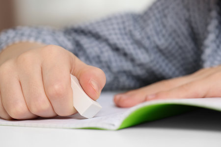 Boy erasing mistake in his notebook at white desk, closeupの写真素材