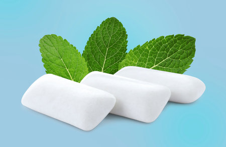 Menthol chewing gum pillows and mint leaves on light blue backgroundの写真素材