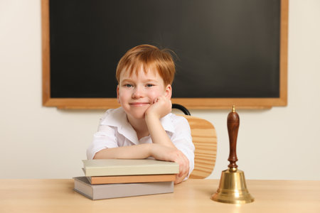 Cute little boy with books and school bell in classroomの写真素材