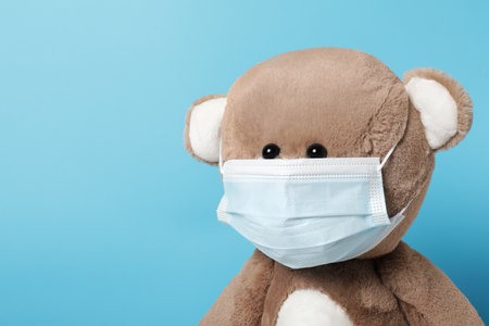 Cute teddy bear in mask on light blue background, space for textの写真素材