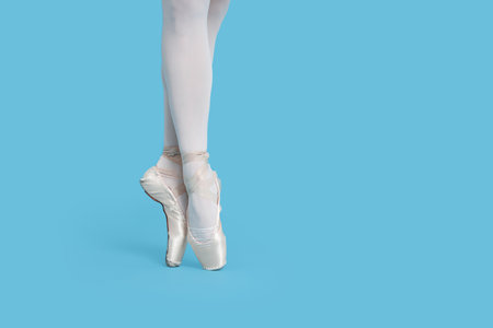 Young ballerina in pointe shoes practicing dance moves on light blue background, closeup. Space for...