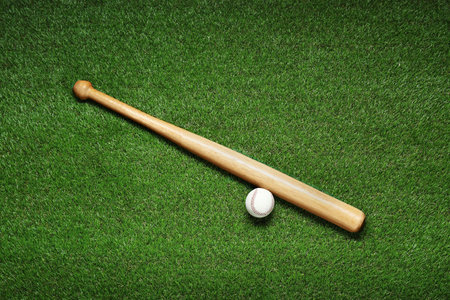 Wooden baseball bat and ball on green grass, flat lay. sports equipment